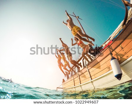 Group of happy friends diving from sailing boat into the sea - Young people jumping inside ocean in summer vacation - Main focus on right man - Travel and fun concept - Fisheye lens distortion