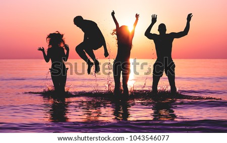 Happy friends jumping inside water on tropical beach at sunset - Group of young people having fun on summer vacation - Youth lifestyle, party and friendship concept - Focus on bodies silhouette