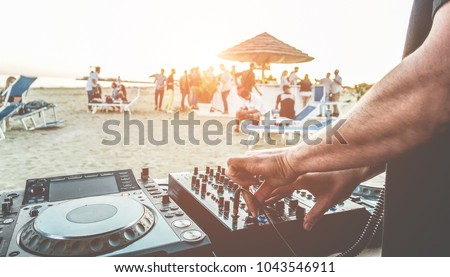 Dj mixing at sunset beach party in summer vacation outdoor - Disc jockey hands playing music for tourist people in chiringuito kiosk bar - Event, music and fun concept - Focus on left hand
