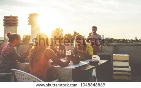 Young friends having barbecue party at sunset on penthouse patio - Happy people doing bbq dinner outdoor cooking meat and drinking wine - Focus on right woman - Food, fun and friendship concept