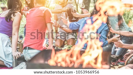 Happy friends having picnic dinner with barbecue in nature outdoor - Young people eating bbq meal and toasting wine - Focus on behind left guys - Youth lifestyle, summer and friendship concept