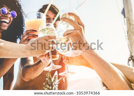 Group of happy friends cheering with tropical cocktails at boat party - Young people having fun in caribbean sea tour - Youth and summer vacation concept - Focus on bottom hands glass