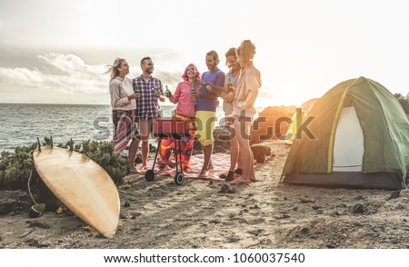 Happy friends drinking beers at camping barbecue picnic next to the ocean - Surfers people having fun and laughing together - Main focus on right guys - Travel, vacation and friendship concept