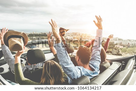Happy friends with hands up having fun in convertible car on summer vacation - Young people laughing and smiling together during travel holidays - Youth lifestyle concept - Main focus on right guys