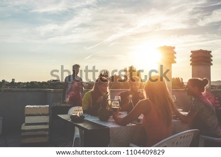 Young friends having barbecue party at sunset on penthouse patio - Happy people doing bbq dinner outdoor cooking meat and drinking wine - Focus on left woman face - Food, fun and friendship concept