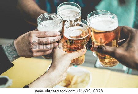 Group of friends enjoying a beer in brewery pub - Young people hands cheering at bar restaurant - Friendship and youth concept - Main focus on left bottom hands