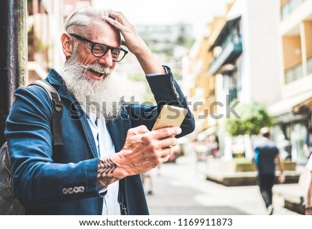 Trendy senior man using smartphone app in downtown center outdoor - Mature fashion male having fun with new trends technology - Tech and joyful elderly lifestyle concept - Focus on his face