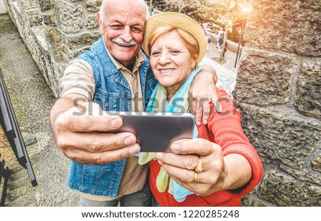 Senior couple taking a selfie inside castle on tour vacation - Mature husband and wife having fun with technology trends - Love, relationship and joyful elderly lifestyle concept - Focus on faces