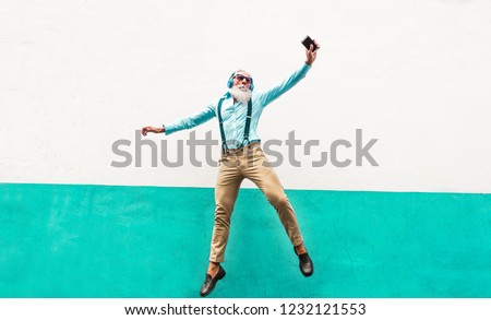 Crazy senior man jumping and listening music outdoor - Happy mature male celebrating and dancing outside - Joyful elderly lifestyle and technology concept - Focus on him