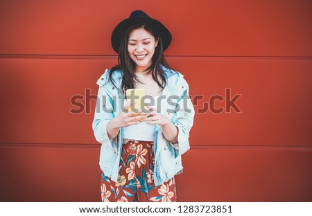 Asian social influencer woman using smartphone with coral background - Happy chinese girl having fun with new trends technology - Fashion, tech and millennial generation activity - Focus on face