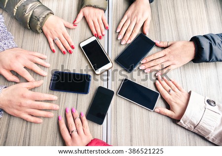 Group of friends having fun together with smartphones - Closeup of hands social networking with mobile cellphones - Technology and phone addiction concept on wood background - Focus on mobile phones