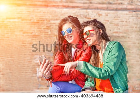 Best fashion addicted friends watching videos surprised on smartphone- Girlfriends having fun outdoors - Technology addiction concept - Main focus on right girl\'s face with artificial sunlight