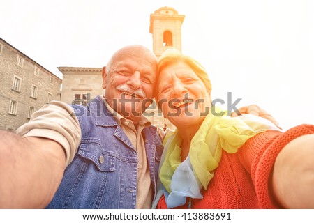 Senior couple taking a selfie in old town center - Two persons in the 60\'s having fun with new technologies outdoor at sunset - Concept of active elderly and fun around the world -
