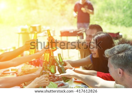Group of multiracial students having barbecue on a sunny day - Young cheerful people cheering with beer bottles on summer time - Concept about good and positive mood with friends - Focus on blonde guy