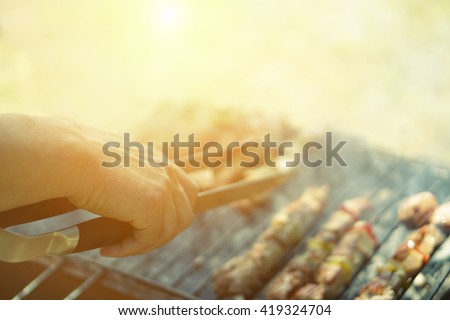 Young man cooking meat on barbecue - Chef putting some meat skewers on grill in park outdoor - Concept of eating outdoor during summer time - Vintage retro filter with sun halo flare
