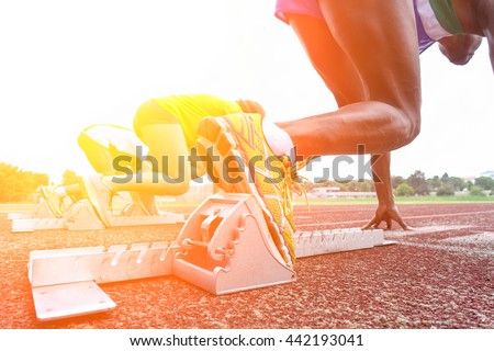 Runners feet on starting blocks in a athletic running track - Young multi race people training outdoor at sunset - Close up on shoe with back lighting - Soft warm filter with focus on first shoe