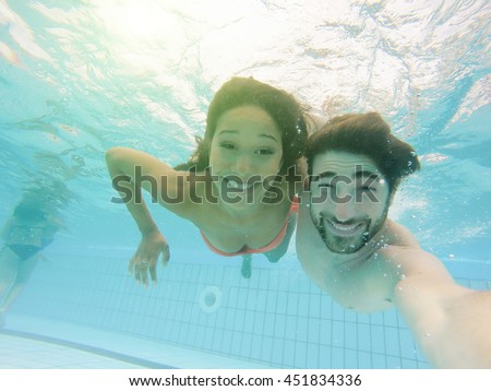 Handsome couple taking selfie under the water in swimming pool resort with back lighting - Young people having fun during vacation - Technology addiction concept - Warm filter