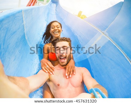 Young happy friends having fun in aqua park pipe with camera - Cheerful multi race couple taking selfie photo with funny faces - Vacation and love concept - Soft saturated filter