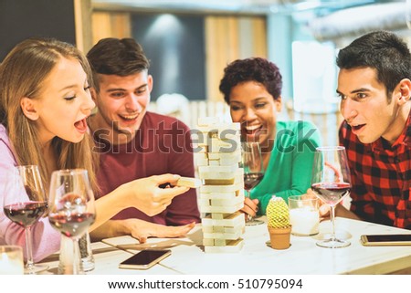 Group of young friends having fun playing wood board game in pub wine shop - Multiracial cheerful people smiling and enjoying time together indoor - Friendship concept - Focus on left girl eye
