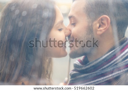 Portrait of young couple in love kissing under the rain with transparent umbrella - Handsome man and woman enjoying first date - Tender moments concept - Focus on girl face - Warm vintage filter