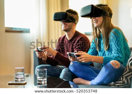 Young happy couple playing video games virtual reality glasses in their apartment - Cheerful people having fun with new trends technology - Gaming concept - Focus on woman headset