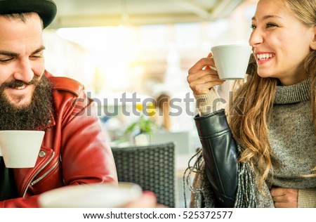 Happy friends toasting coffee and cappuccino at bar restaurant cafe  - Young hipster people enjoying breakfast drinking hot beverage - Friendship winter concept - Focus on woman eye - Warm filter