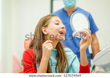Young woman checking their teeth at mirror after dental treatment - People bodycare and stomatology concept for healthy lifestyle - Focus on girl face - Warm filter with soft vivid editing