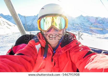 Happy skier taking selfie photo with smart cell phone camera sitting on ski lift - Young man having fun in winter snow resort vacation with back light - Sport concept - Warm filter