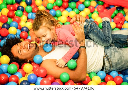 Young father playing with his daughter inside ball pit swimming pool - Happy people having fun in children playground indoor - Family and love concept - Focus on man face - Warm vivid filter