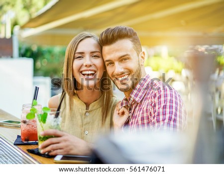 Happy couple toasting cocktails in lounge disco bar for summer vacation - Young people having fun with new mixology club beverage - Party and happy hour concept - Focus on woman face - Warm filter