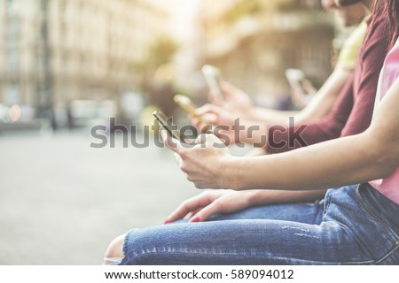 Group of teenagers friends watching mobile phones in city - Young people addiction to technology trends - Alienation moment for new generation problem - Focus on first hand - Warm cinematic filter