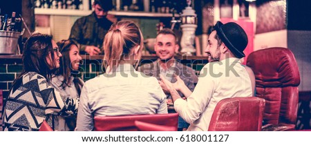 Group of young trendy friends chatting and laughing together inside cocktail fashion bar - Cheerful people having fun doing pre dinner appetizer - Focus on right man face - Vintage filter