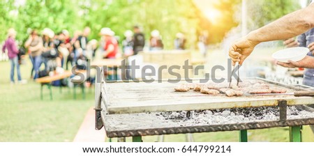 Man cooking bbq meat at festival outdoor - Chef grilling sausages in park outside - Concept of summer party with families  and friends - Focus on hand tongs - Warm filter