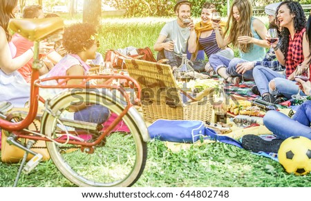 Diverse culture friends making picnic on city park outdoor - Young trendy people drinking wine and laughing outside - Focus on man with hat and two girls next him - Youth concept - Contrast filter