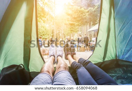 Pov view of happy couple inside tent at camping wood festival - Young people having fun on summer vacation into the wood - Travel,love,nature concept - Main focus on left feet - Warm contrast filter