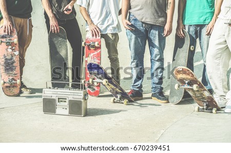 Young friends holding skateboards in hands outdoor on city skate park  - Teen friends having fun skating and listening music outside - Extreme sport,friendship,youth concept - Contrast retro filter