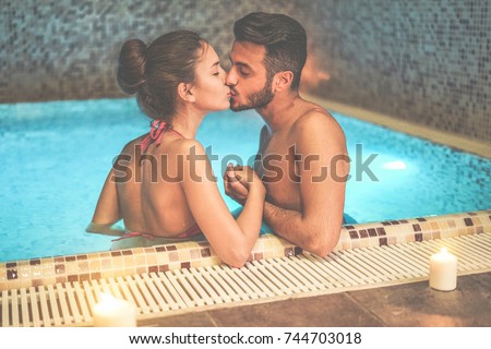 Couple of lovers kissing in spa swimming pool - Romantic love story on vacation resort hotel - Relationship concept with boyfriend and girlfriend together - Focus on woman eye - Warm contrast filter