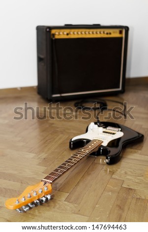 Black electric guitar on the floor, with big amp in the background