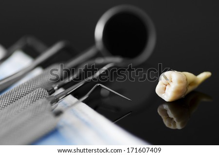 Dental instruments with mask and extracted tooth on black