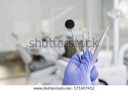 Gloved hand holding dental instruments in dental office