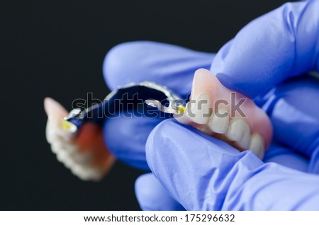 Gloved dentist hand, holding dental prosthesis on black background