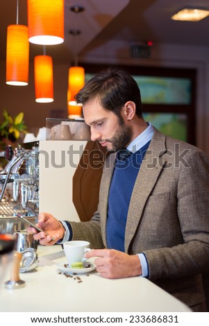 Business man in coffee shop, drinking espresso and holding his phone