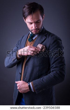 Handsome man in suit with tie and pocket square, fixing his pocket square, on dark gray background
