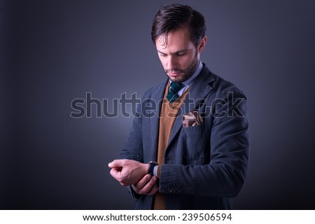 Handsome man in suit with tie and pocket square, looking at his watch, on dark gray background