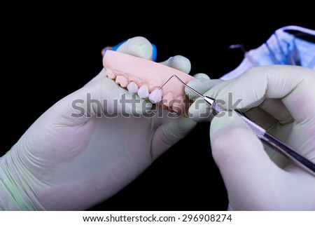 Gloved dentist hand, holding dental prosthesis on black background