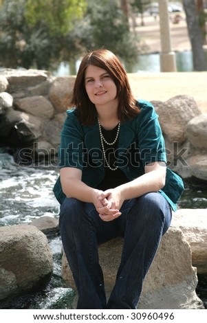 Girl in blue sweater sitting on a rock by a rocky stream