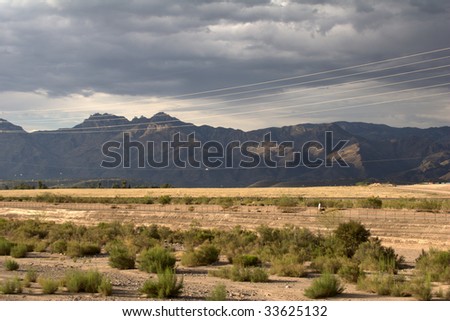 Dark mountains with a bright landscape and dark cloudy skies, with power lines running parallel to the image, showing depth