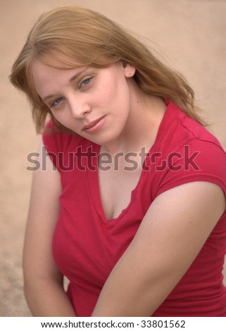 A Gorgeous young woman with blue eyes and long brown hear wearing a red shirt looks longingly at the camera