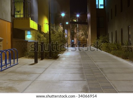 A quiet looking sidewalk between two buildings taken at night time