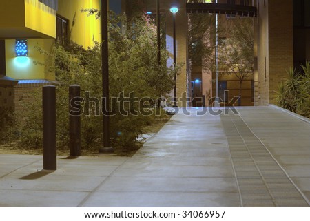 A sidewalk between buildings well lit up at night time.